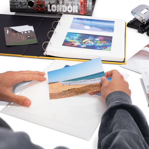 Eine Person hält ein Foto von einem Strand in der Hand, während sie ein Fotoalbum und verschiedene Dokumente auf einem Tisch betrachtet.
