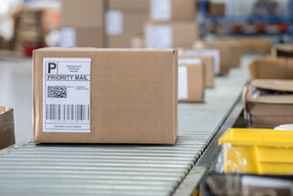 A brown box with a priority mail shipping label on a conveyor belt in a shipping center.