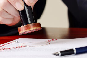 A hand stamps a document with a red stamp on a table, next to it are a blue pen and a black stamp.