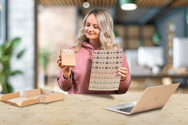 A woman is holding a drink in one hand and a patterned sheet in the other while sitting at a table.