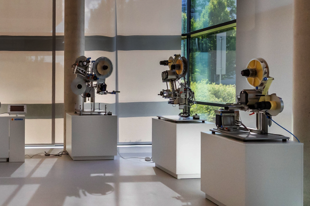 Exhibition of machine models on white pedestals in a modern space with large windows and natural light.