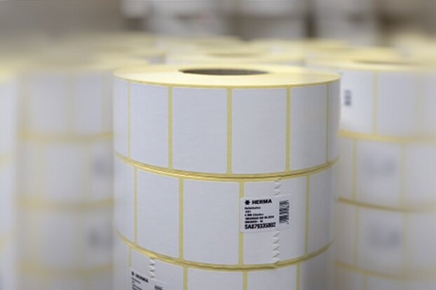 Rolls with white labels, stacked in a storage environment. The labels are marked with yellow lines.