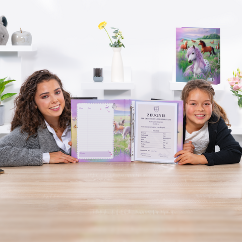 Two girls are sitting at a table, holding an open notebook with a certificate and a blank page. Decorative elements are visible in the background.