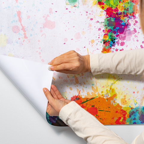 Hands are pulling a colorful, vibrant wallpaper from a roll as it is being applied to a wall.
