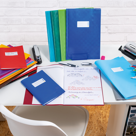 Colorful binders and notebooks on a desk, next to a pen and a stapler. An open notebook with handwritten notes is visible.