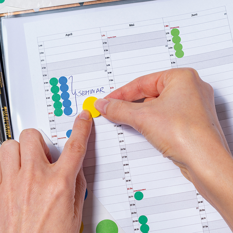 Ein Hand, die einen roten Punkt auf einem Kalender für September und Oktober anzeigt, mit hervorgehobenen Daten und Wochentagen.