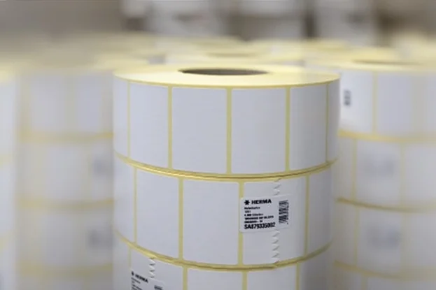 Rolls with white labels, stacked in a storage environment. The labels are marked with yellow lines.