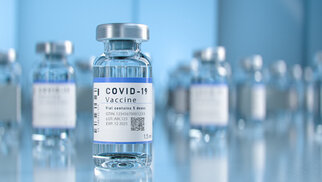 COVID-19 vaccine vials on a table, containing a clear liquid and a label with important information.