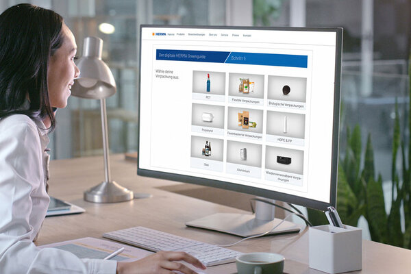 A person in a white lab coat is sitting at a desk, looking at a computer screen displaying various product options.
