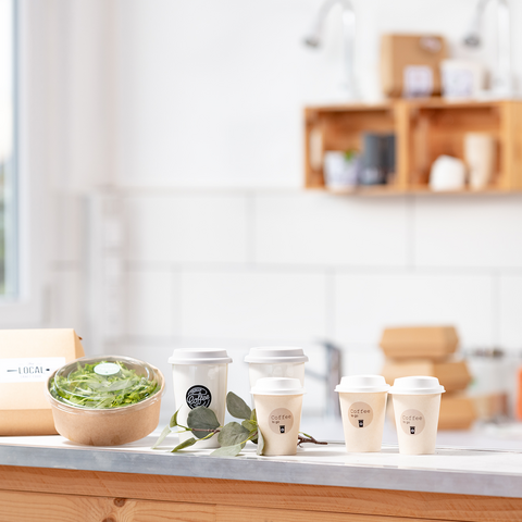 A wooden table with a bowl of salad, several coffee mugs, and a package, surrounded by a bright, modern kitchen.