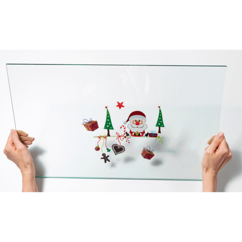Eine transparente Glasplatte wird von zwei Händen gehalten, mit festlichen Motiven wie einem Weihnachtsmann, Tannenbäumen und Geschenken.
