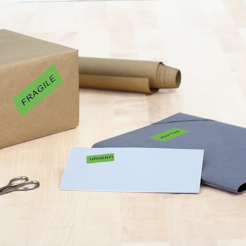 A box with the label 'FRAGILE,' next to an envelope marked 'URGENT!' and a roll of wrapping paper on a table.