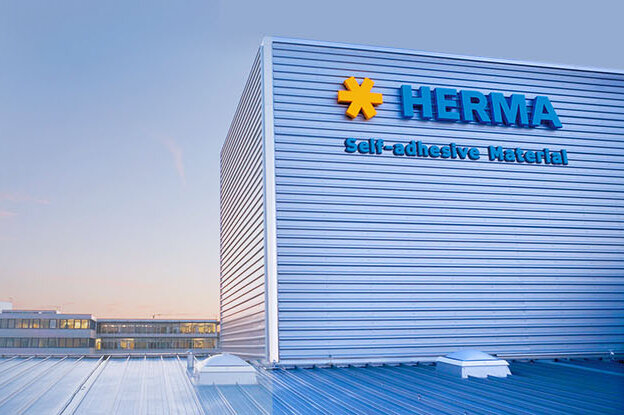 The building with the sign 'HERMA' and a blue sky in the background. The architecture is designed to be modern and functional.