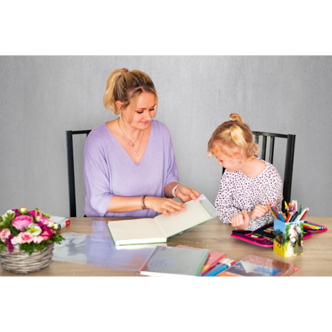 Eine Frau und ein Kind sitzen an einem Tisch und schauen gemeinsam in ein Buch. Auf dem Tisch liegen weitere Bücher und Bastelmaterialien.