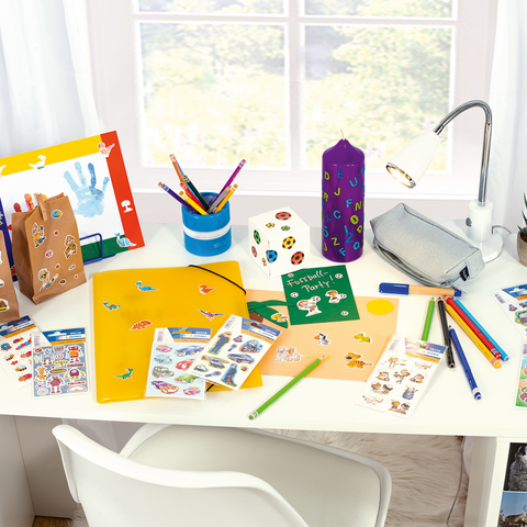 Colorful crafting materials on a table, including stickers, markers, a die, and a yellow notebook featuring dinosaur designs.