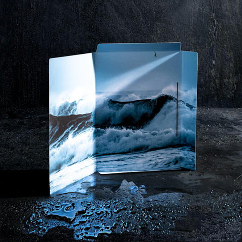 Eine offene Mappe mit einem Bild von Wellen, die gegen die Küste schlagen, auf einem dunklen, nassen Untergrund.