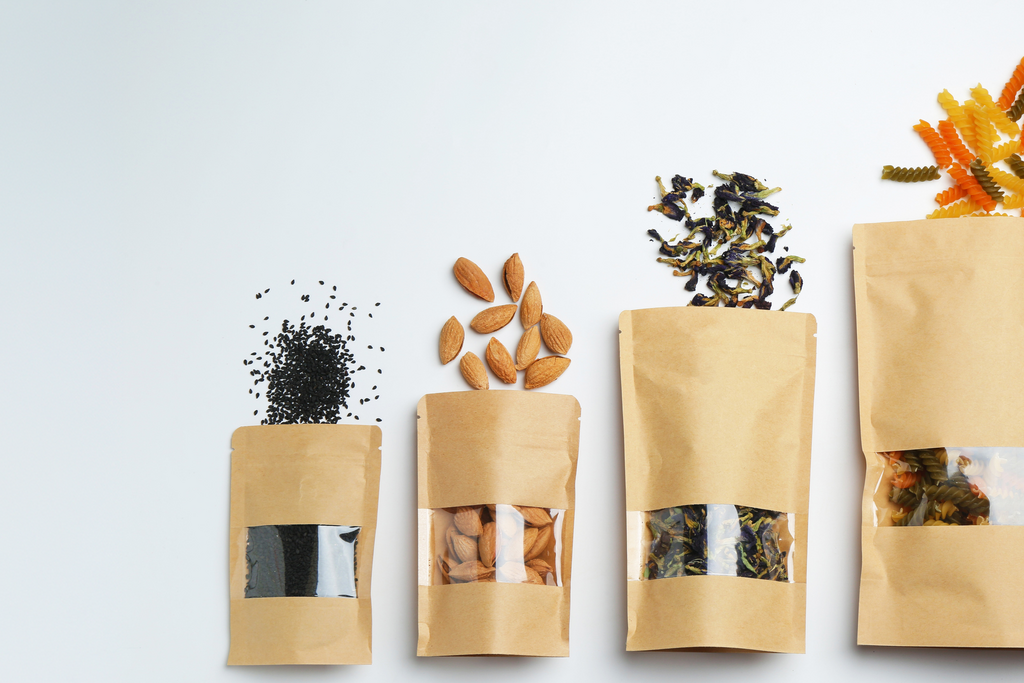 Five brown paper bags filled with various dried herbs and plants, lined up in a row.