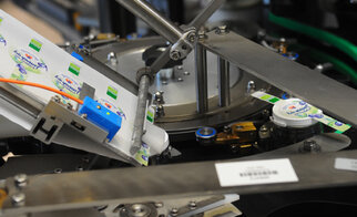 Machine for labeling bottles, with a label applied to a cap. Mechanical parts are visible.