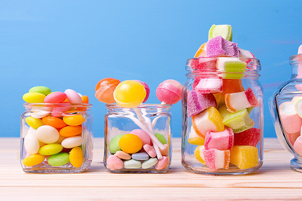 Colorful candies in various jars on a wooden surface, set against a blue background.