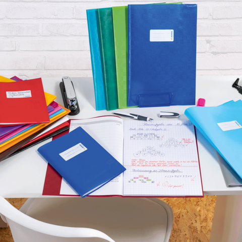 Eine Frau und ein kleines Mädchen sitzen an einem Tisch und blättern in einem Heft. Bunte Stifte und ein Notizbuch liegen auf dem Tisch.