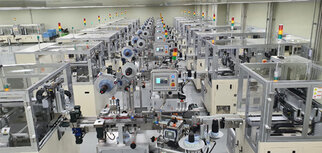Factory hall with several automated machines set up for production, equipped with monitors and control units.