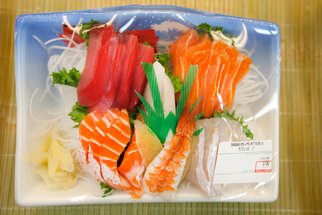 A sushi platter with various types, including salmon, tuna, and shrimp, served on a plate with sides like ginger and vegetables.