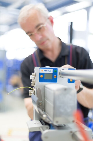 A man is operating a device from HERMA that is used for labeling. The focus is on the control panel of the device.