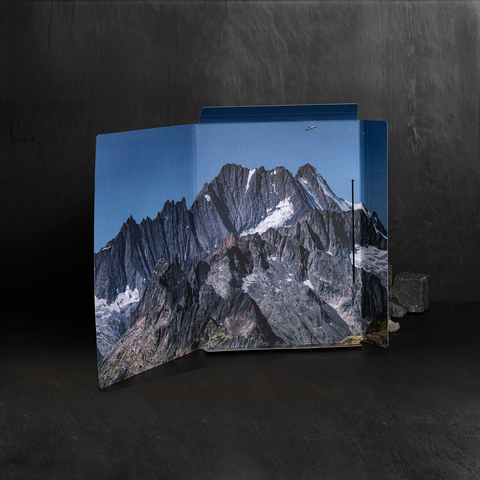 Ein aufgeschlagener Ordner mit einem Bild von schroffen Bergen und schneebedeckten Gipfeln. Der Hintergrund ist dunkel und neutral.