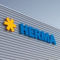Yellow star logos and blue letters form the word 'HERMA' on the exterior wall of a modern building.