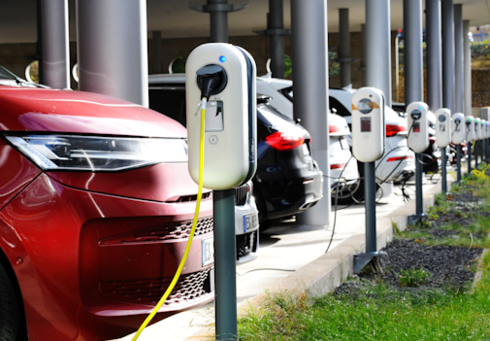 Several electric cars are at charging stations while they are being charged. The vehicles come in various colors and models.