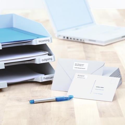 Folder with labeled sections for incoming and outgoing documents, next to it are envelopes and a postcard on a table.