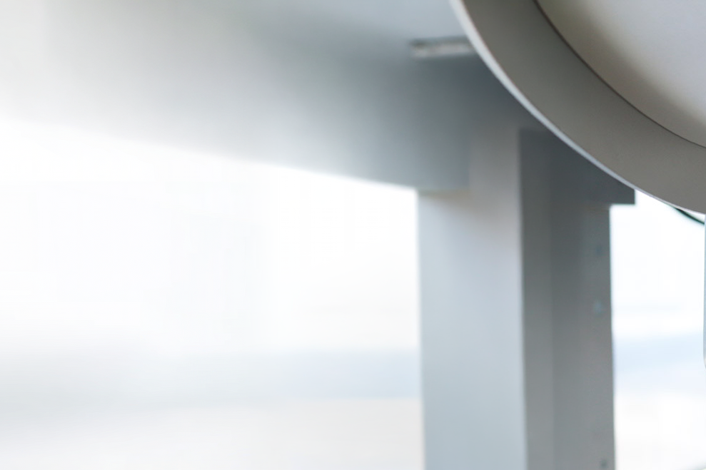A machine component with a roller that unwinds a white material, set against a bright, blurred background.
