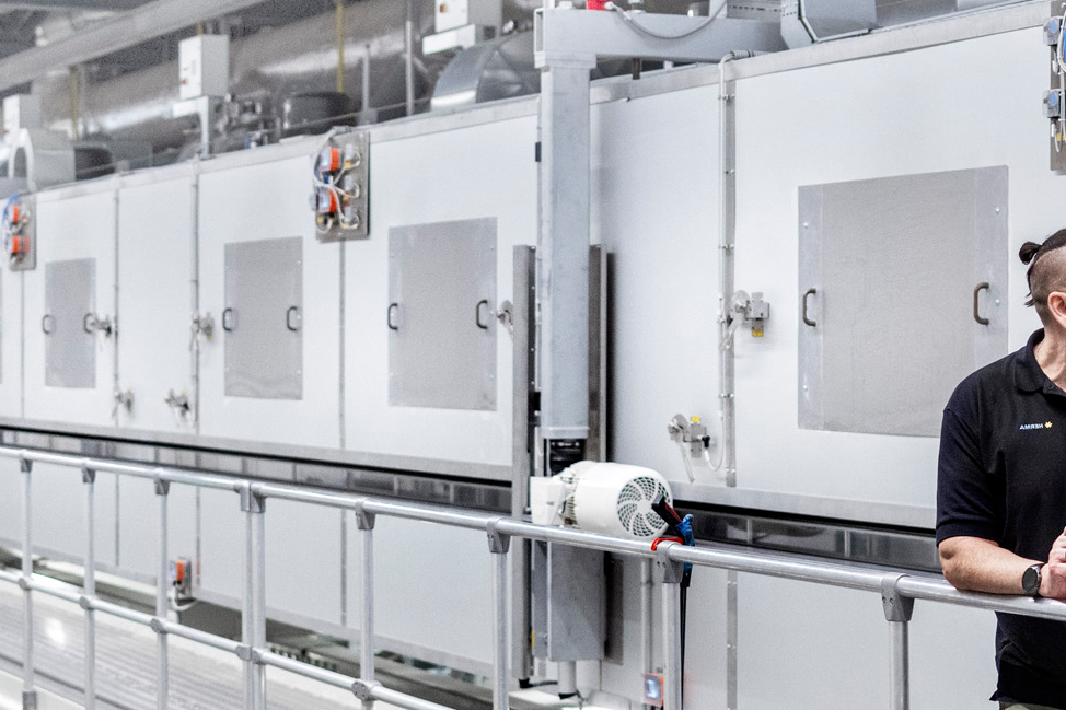 Two men are standing in a modern industrial setting, discussing technical details in front of a row of machines.