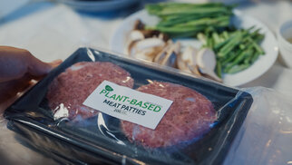 A hand holds a package of plant-based meat patties, while sliced mushrooms and green beans are in the background.