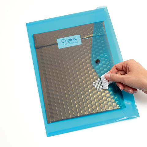 A hand holds a blue padded shipping envelope with a silver lining and a sticker that says 'Original.