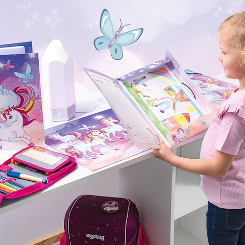 A girl flips through a folder filled with colorful drawings, surrounded by markers, a backpack, and a nightlight.