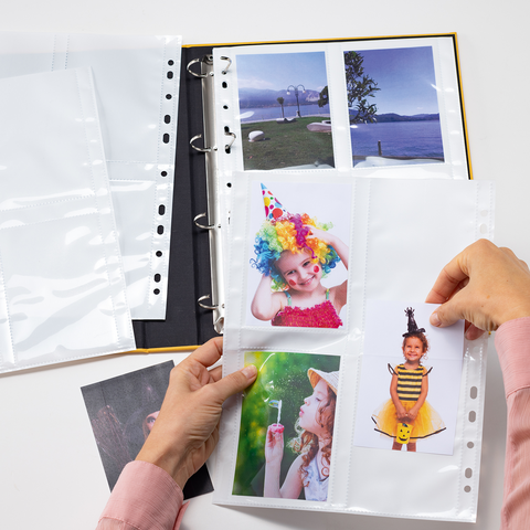 Ein Fotoalbum mit mehreren leeren und gefüllten Hüllen, in denen Bilder von Kindern mit Partyhüten und bunten Accessoires aufbewahrt werden.