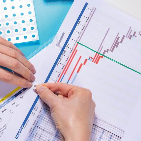 A hand places a sticker on a document filled with charts and tables, while another hand holds the sheet.