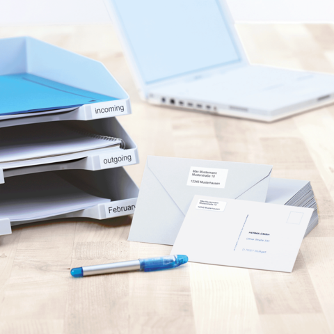 Ordner mit beschrifteten Fächern für eingehende und ausgehende Dokumente, daneben Briefe und ein blauer Stift auf einem Tisch.