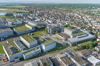 Aerial view of a modern commercial area featuring several buildings with green roofs, surrounded by residential neighborhoods and landscape.