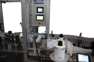 Automatic labeling machine with multiple rolls, control unit, and labels on bottles.
