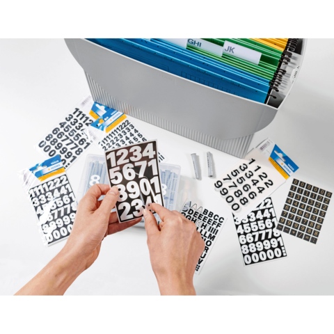 Hände halten ein Blatt mit Zahlenaufklebern, umgeben von weiteren Aufklebern und einem Ordner mit farbigen Trennblättern.