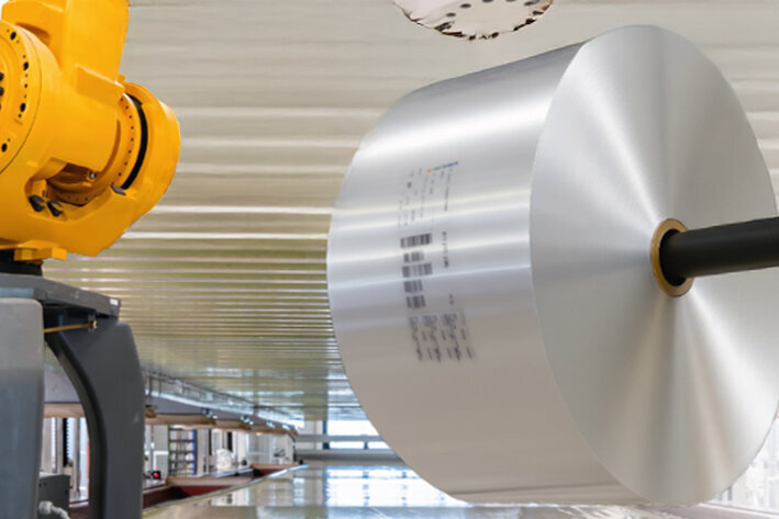 A yellow industrial robotic arm is assembling a large, silver component in a modern manufacturing environment.