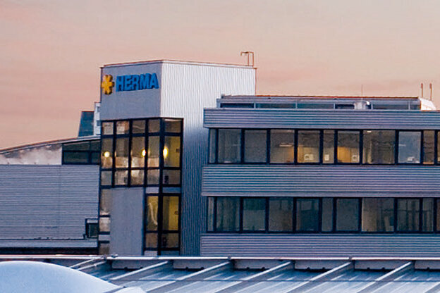 Modern office buildings with large windows and a clear, functional design, surrounded by an urban environment at dusk.