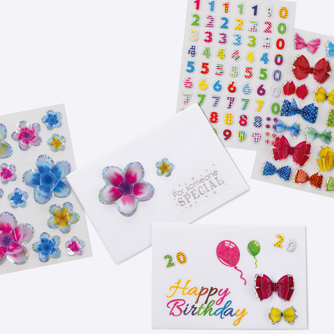 Bunte Aufkleber mit Blumen, Zahlen und Schleifen, sowie eine Geburtstagskarte mit der Aufschrift "Happy Birthday" und Luftballons.
