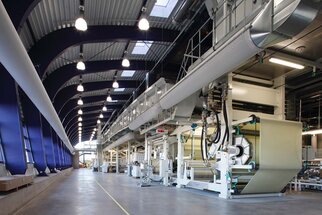Modern production hall with large machines for processing materials, bright lighting, and high ceilings.