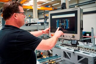 A man is using a touchscreen in a factory that displays information about machines and production data.