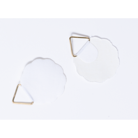 Zwei weiße, blütenförmige Stoffstücke mit goldenen Clips.