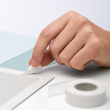 A hand removes a piece of tape from a gray surface, while another piece of tape lies nearby.