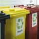 Drei Abfallbehälter in verschiedenen Farben für Recycling: Gelb für Plastik, Rot für Glas und Schwarz für Restmüll.